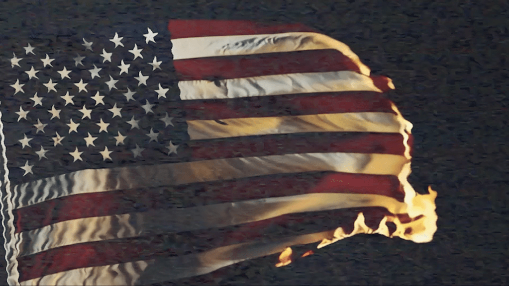 Image of an American flag burning, with flames consuming the fabric against a dark background.